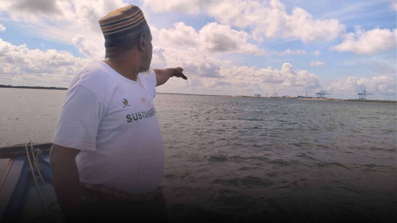 Abubakar Mohammed Twalib standing on a boat gesturing toward the shore